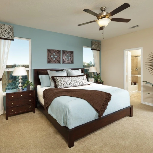 A cozy bedroom with a light blue accent wall behind a dark wood bed. The remaining walls are painted a warm beige.