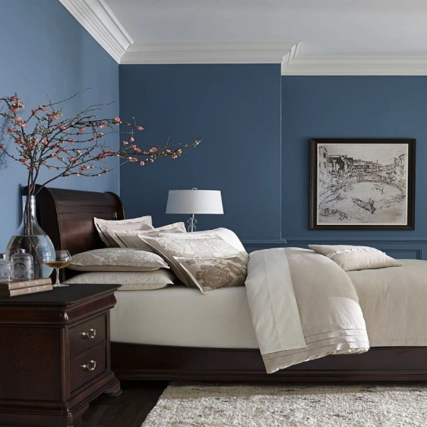 A serene bedroom with deep blue painted walls and white crown molding. A dark wood sleigh bed with neutral-toned bedding and decorative pillows is the main feature.