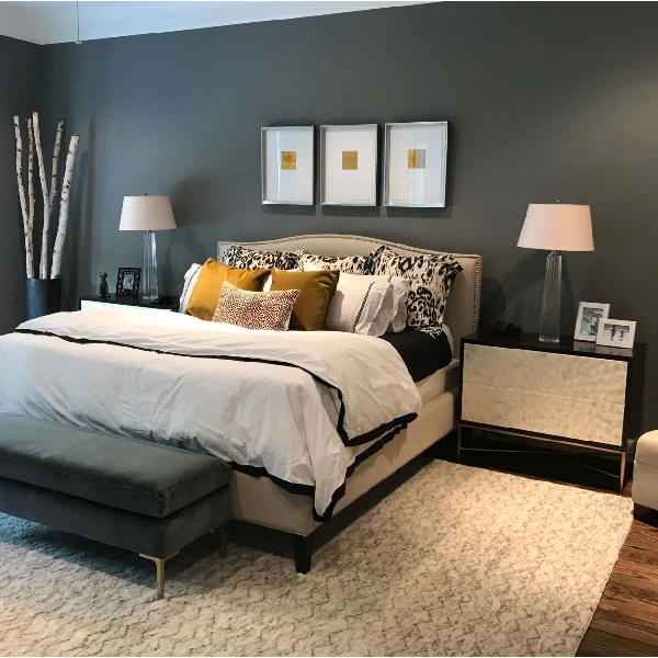 A stylish bedroom painted in a sophisticated dark grey. A light-colored upholstered bed with patterned and solid pillows is the focal point.